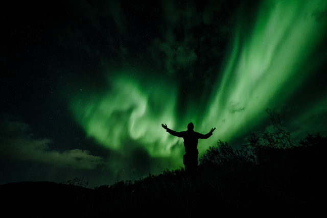 Silhouette humaine se d&eacute;tachant sous des aurores bor&eacute;ales dans le ciel nocturne de Norv&egrave;ge